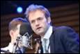 A person in a suit speaking into a microphone

Description automatically generated