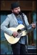 A person playing guitar and singing into a microphone

Description automatically generated