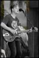 A person playing guitar and singing into a microphone

Description automatically generated