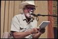 A person in a cowboy hat holding a paper and a microphone

Description automatically generated